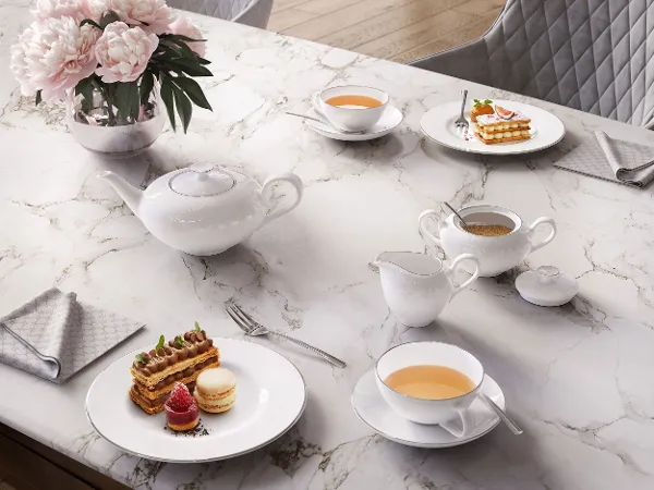 Elegant Anmut theeservies op een marmeren tafel, bestaande uit een theepot, kopjes en melkkannetje met thee en koekjes.