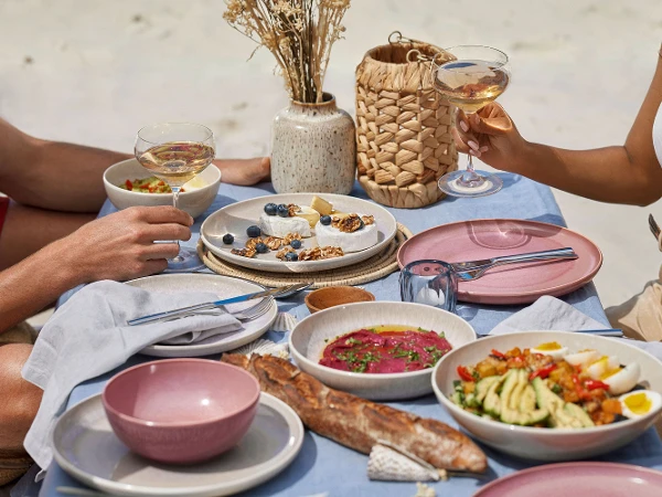 On a beach, a couple is sitting at a table with plates from the Perlemor collection from like. by Villeroy & Boch.