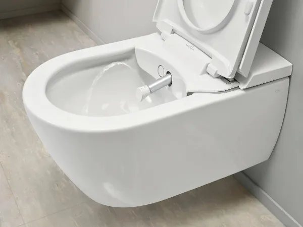 Un gros plan sur des toilettes modernes suspendues au mur avec un couvercle ouvert et un jet d’eau sortant de la cuvette.