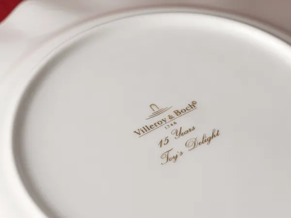 Bottom stamp of the Toys Delight collection by Villeroy & Boch The underside of a white Villeroy & Boch plate with gold lettering and the inscription "15 Years Toy's Delight."