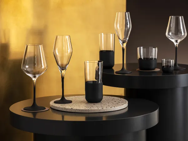 Several elegant Manufacture glasses on modern black tables against a textured golden background.