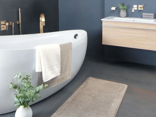 Textiles de salle de bains Villeroy & Boch dans une salle de bains avec une baignoire blanche et un plan de toilette en bois.