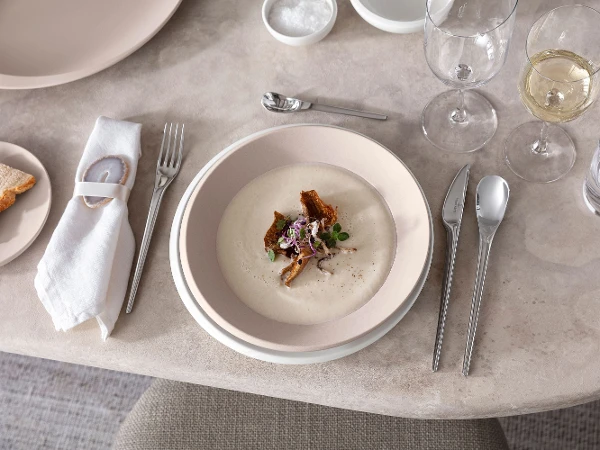 Ein gedeckter Tisch mit NewMoon Tellern und Besteck von Villeroy & Boch mit Cremesuppe.