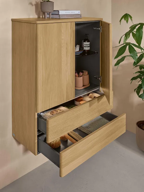 Ein Badschrank aus hellem Holz mit zwei Türen und zwei offenen Schubladen von Villeroy & Boch an einer naturbelassenen Wand.