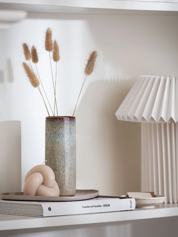 A shelf with a tall Lave vase in beige and a lamp on top.