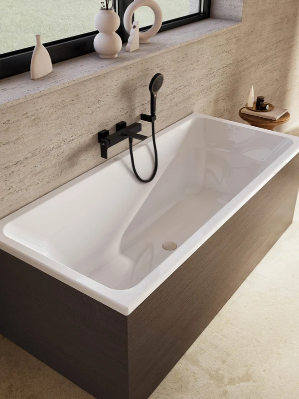 Une baignoire rectangulaire moderne Avento avec un habillage en bois foncé, un robinet mural noir et une douchette à main. La baignoire se trouve à côté d’une grande fenêtre avec des objets décoratifs placés sur le rebord de la fenêtre.