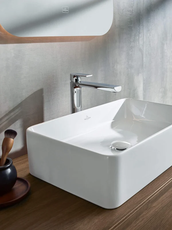 Un intérieur de salle de bains moderne avec un lavabo et des meubles en bois de la collection Collaro avec en arrière-plan une fenêtre avec vue sur la mer.