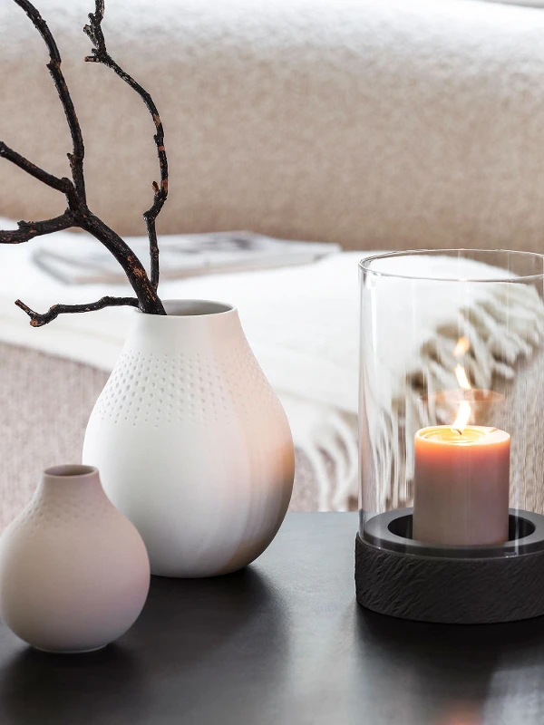 A Manufacture candle stands on a table next to two Manufacture vases.