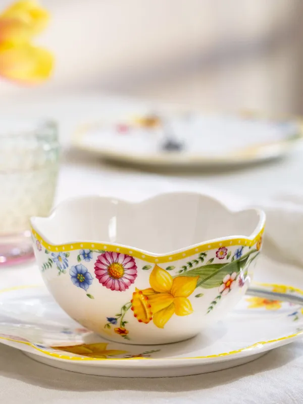 The ‘Spring Awakening’ teacup and saucer with spoon from Villeroy & Boch. The ‘Spring Awakening’ teacup and saucer with spoon from Villeroy & Boch stand on the table next to crystal glasses and softly blurred flowers in the background.