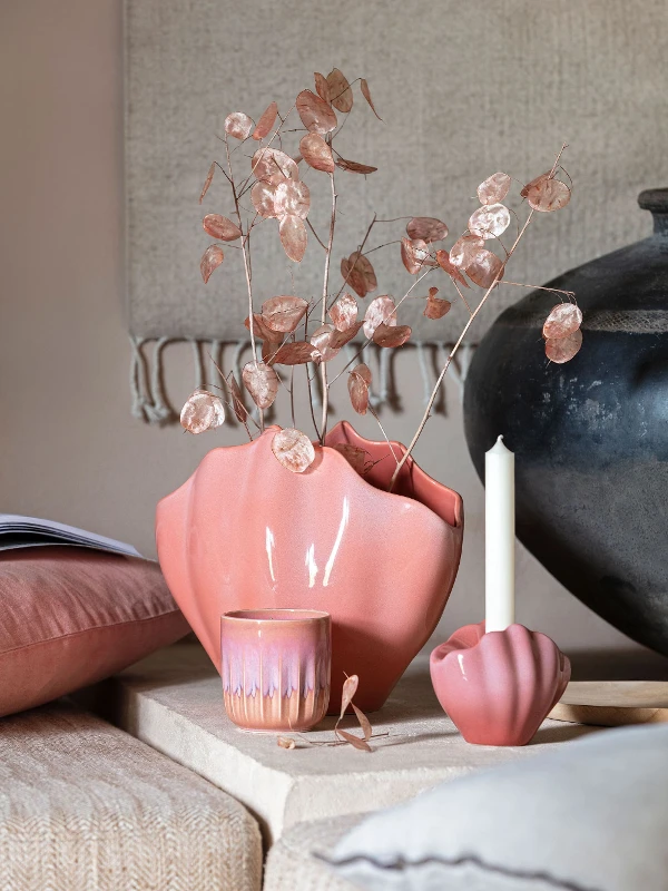 Un vase décoratif Perlemor rose se tient sur une table à côté d’une bougie.