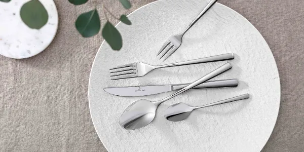 Elegant table decoration with modern Piemont cutlery and decorative greenery on a neutral tablecloth.