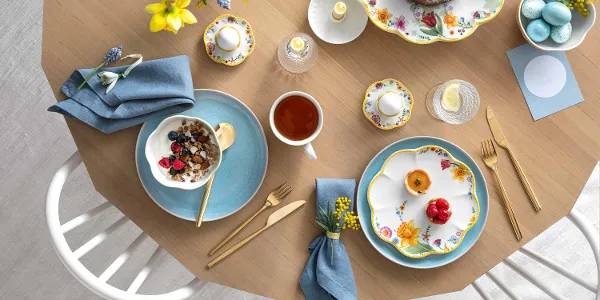 Une table printanière décorée avec de la vaisselle Spring Awakening et Crafted, un kouglof, un plat creux rempli de flocons d’avoine avec des baies, une tasse de thé et des œufs décoratifs.