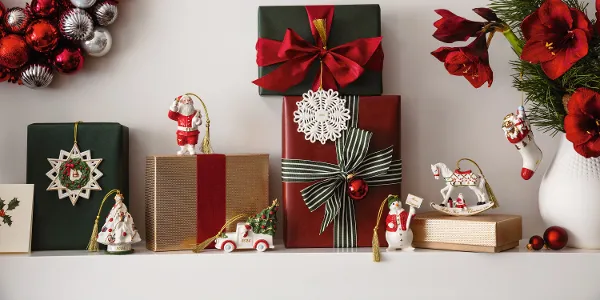 Festive Christmas shelf with wrapped presents, Christmas decorations from Villeroy and Boch, a wreath with red and silver ornaments from Villeroy and Boch and a vase with red flowers and green plants.