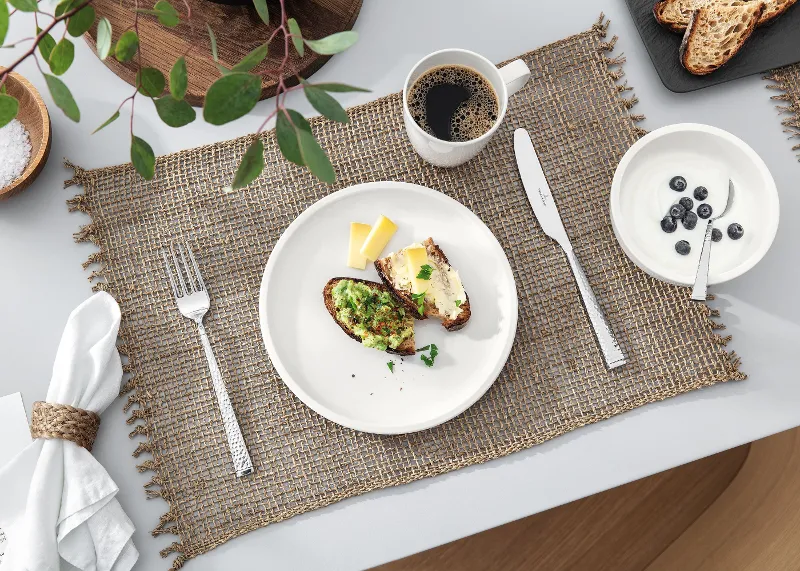 A table set with a cup of coffee and a white Artesano plate from Villeroy & Boch with food.