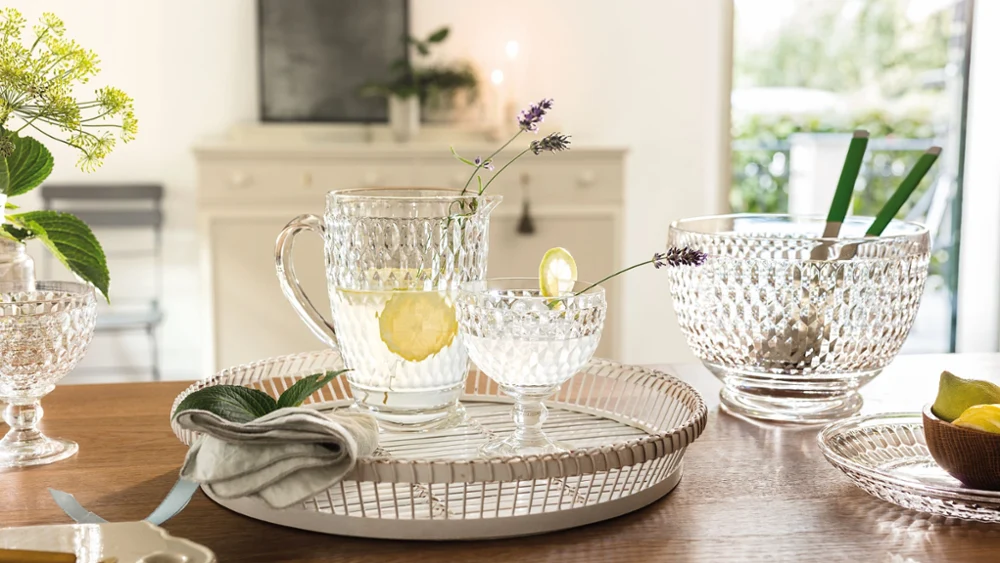 Glasses from Villeroy & Boch with lemon water stand on a tray on a wooden table with glass bowls and a napkin.