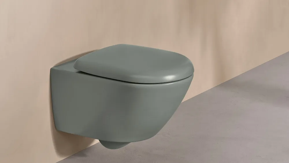 Et Villeroy & Boch WC fra Antao-kolleksjonen i grønt med hvitt betjeningspanel på en naturfarget vegg.