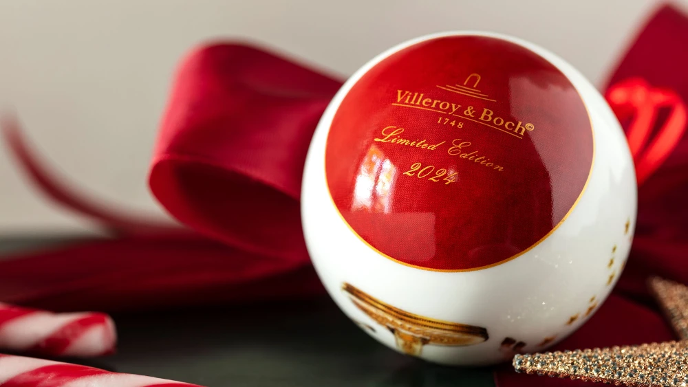 Close-up of a Villeroy and Boch ornament, part of the 2024 limited edition collection, featuring a red and white design with candy canes and a red bow in the background.