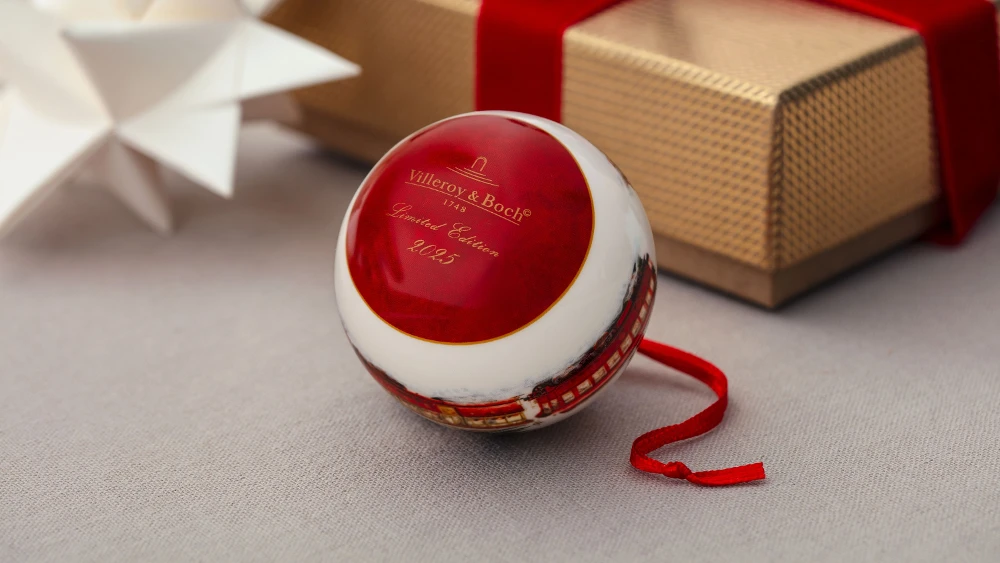 Christmas bauble from the 2025 Annual Christmas Edition collection Red and white Christmas ornaments with the text "Villeroy & Boch" next to a wrapped gift and a white paper star.