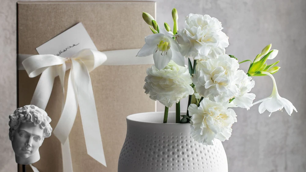 Eine großzügige Manufacture Collier Blanc Perle Vase mit feiner Punktstruktur, verpacktes Geschenk dahinter, ideal für üppige Blumenarrangements.