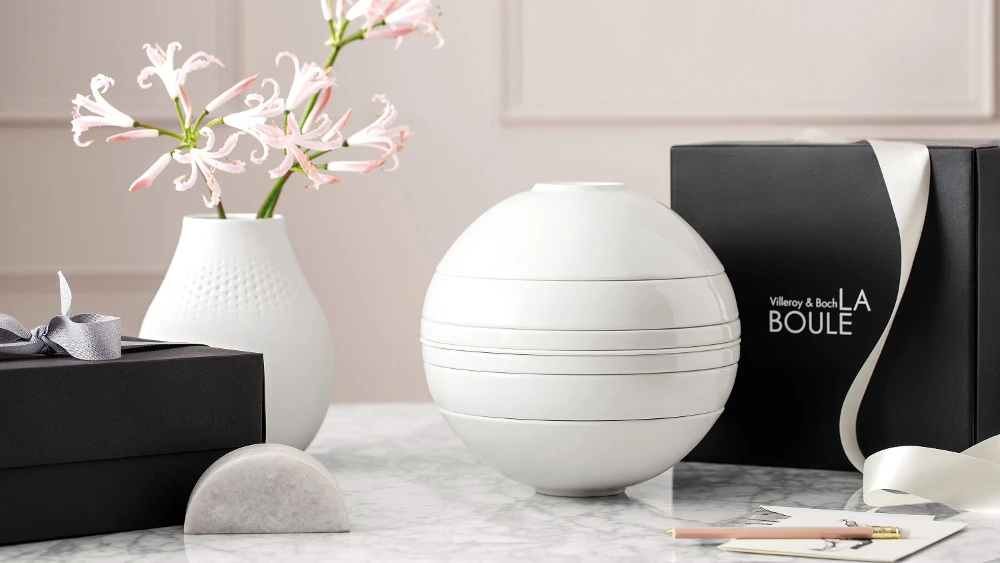 A white La Boule dinnerware set on a table with a black gift box behind it.