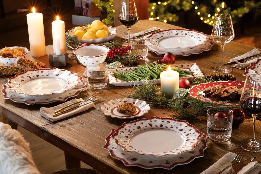 A festive dining table setting with Villeroy & Boch Toy’s Delight patterned plates, glasses and cutlery, with lit candles and Christmas decorations adding the finishing touches to the ambience.