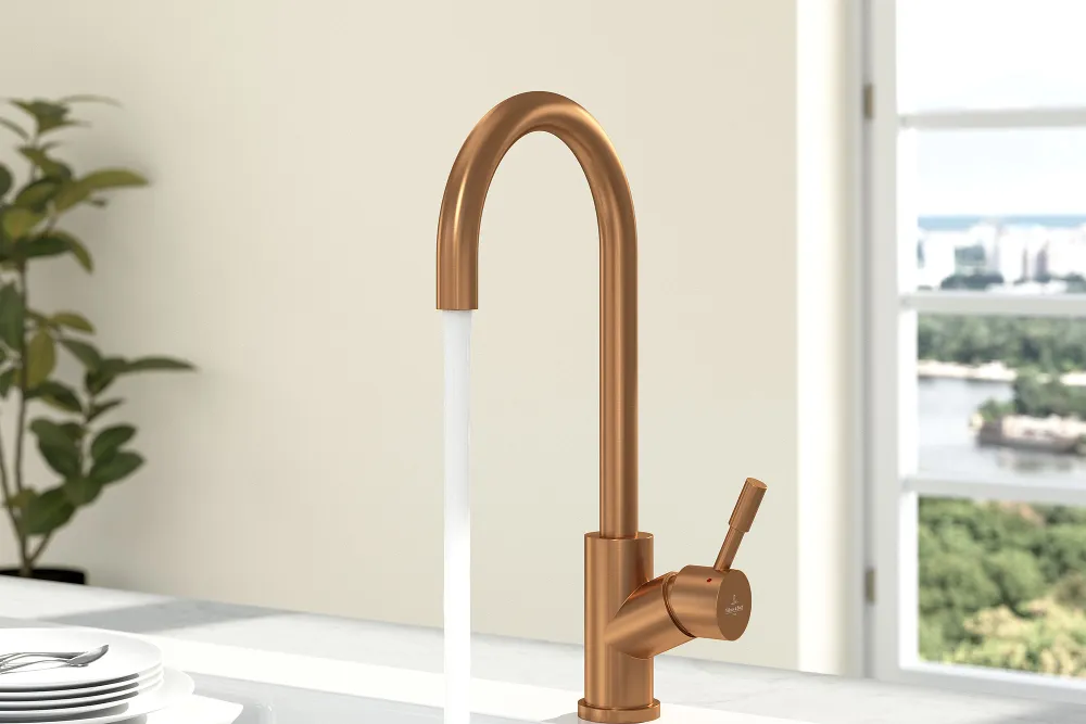 A bronze-coloured umbrella tap on a white sink with white plates on the draining board.