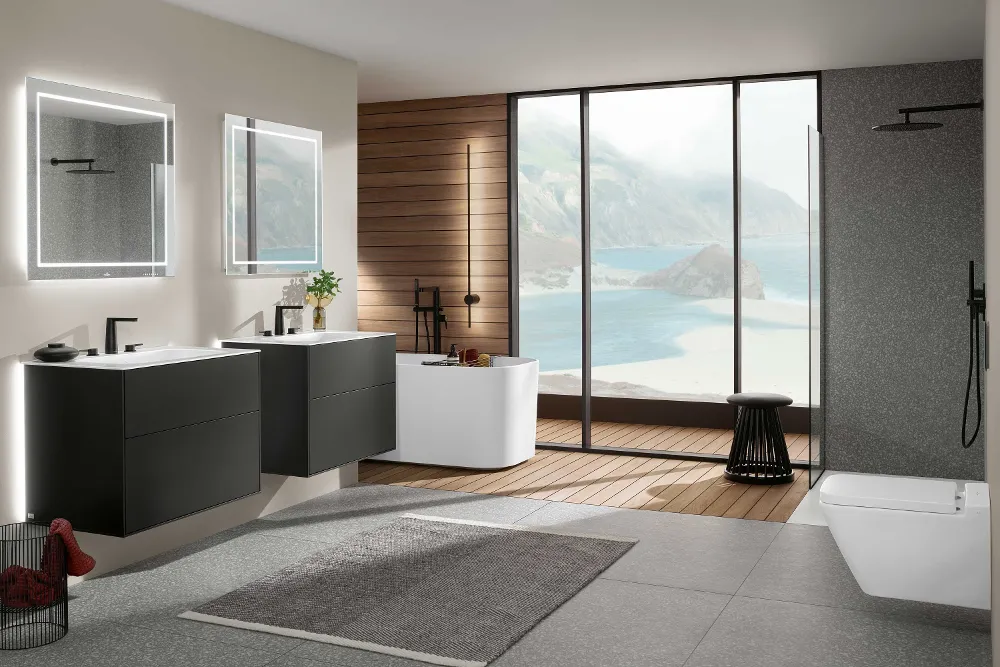 Cuarto de baño Finion con dos lavabos, bañera exenta y ducha acristalada Moderno cuarto de baño con lavabos dobles flotantes Finion, espejos iluminados, bañera exenta, ducha acristalada y grandes ventanales con vistas al mar. Mobiliario minimalista con una mezcla de superficies de madera y piedra.