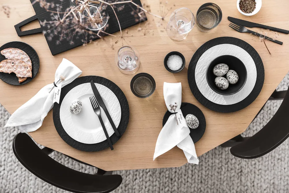 A modern dining table with black and white crockery and cutlery from the Manufacture collection and minimalist Easter decorations.