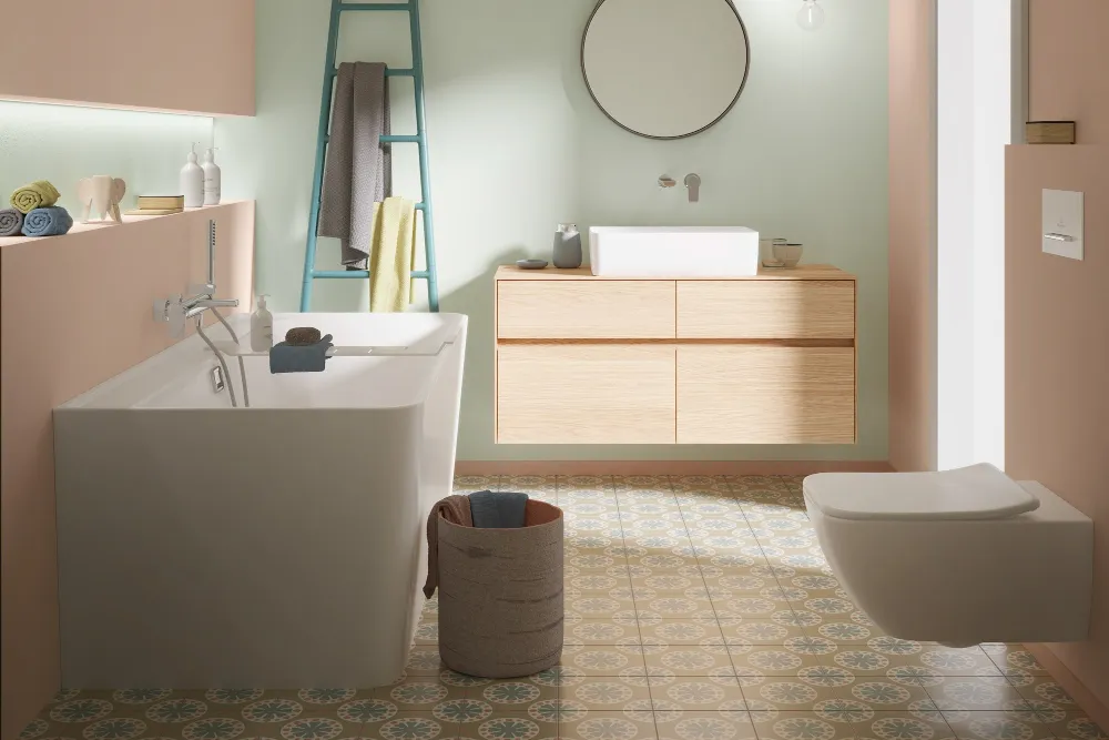 Modernes Badezimmer mit Collaro WC, weißem Waschtisch und einem Waschbeckenschrank in Oak mit rundem Spiegel. Der Boden besteht aus gemusterten Fliesen und die Decke ist mit Holzpaneelen designt.