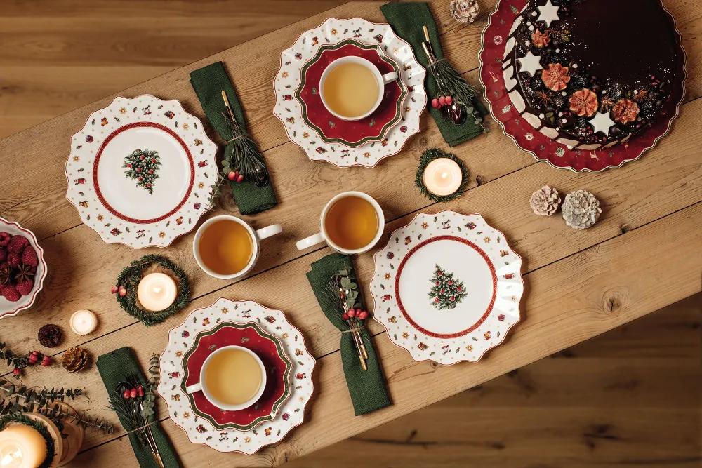 Festive table setting with Toy's Delight plates, cups of tea, a chocolate cake and candles on a wooden table.