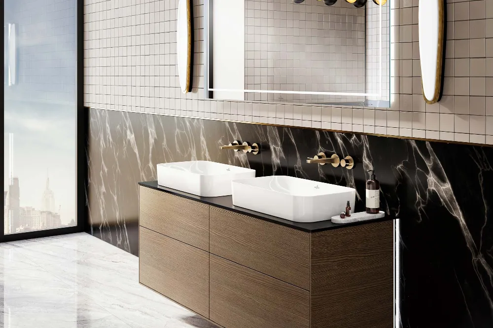 Lavabo doble con espejo grande de la colección Finion Moderno cuarto de baño con lavabo doble Finion, suelo de mármol, detalles de mármol en las paredes, gran espejo y lámparas colgantes. Las ventanas del suelo al techo muestran un paisaje urbano.