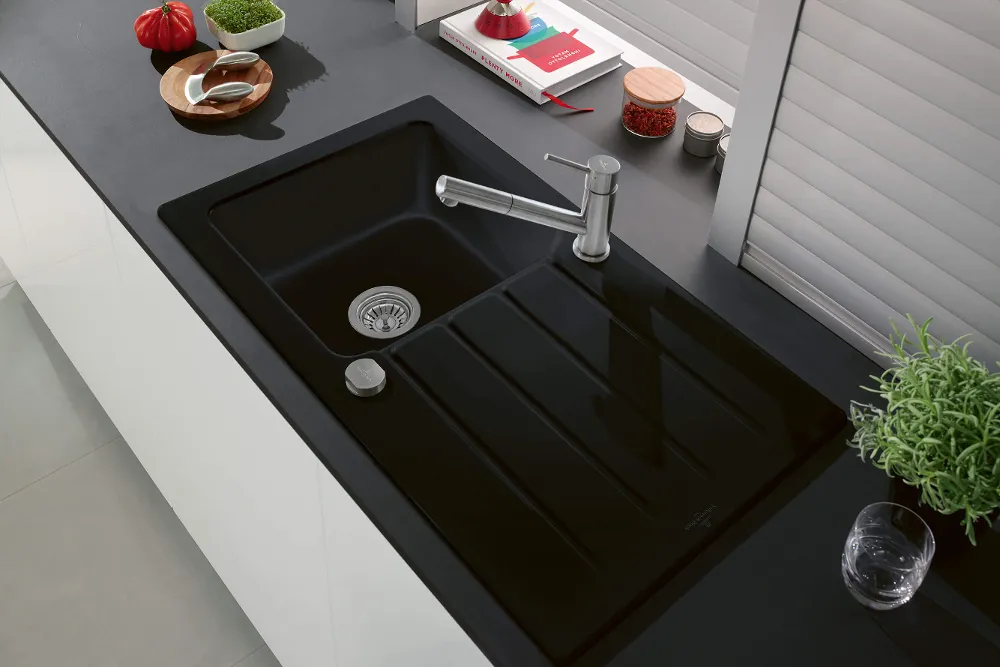 Eine schwarze Küchenspüle aus Keramik mit Chromarmatur in einer Küche mit schwarzer Arbeitsplatte