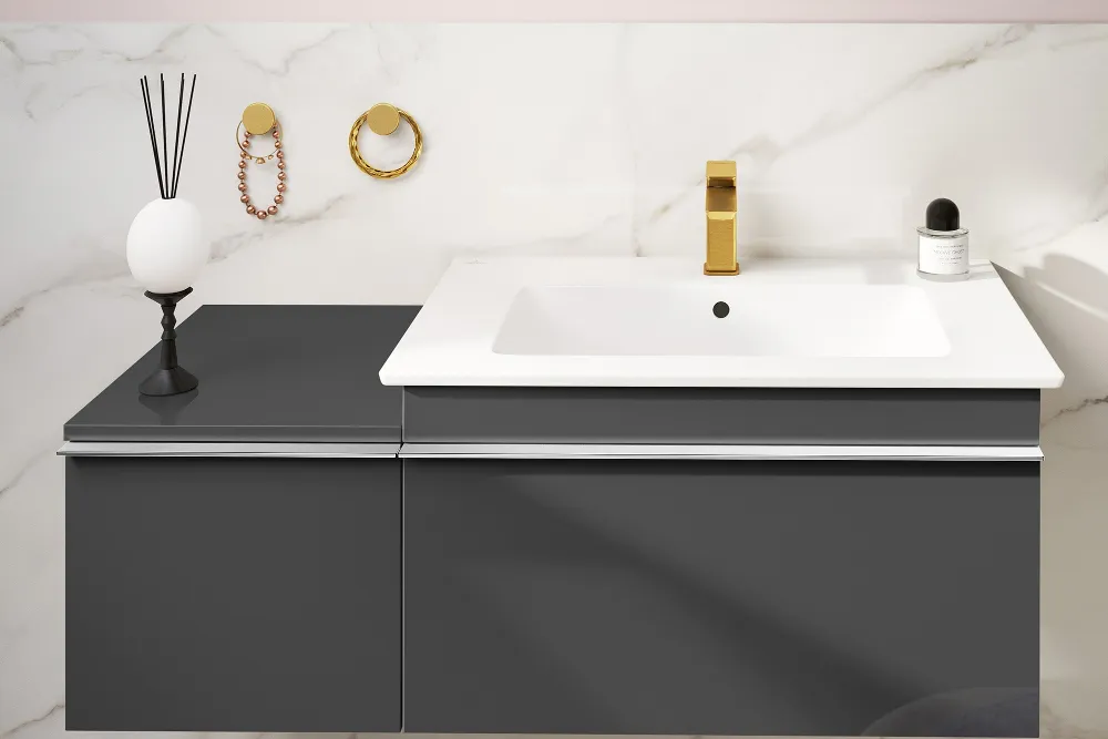 Ein modernes Venticello Waschbecken mit weißer Arbeitsplatte, goldenem Wasserhahn und dunkelgrauem Schrank. Es verfügt über einen runden Spiegel, einen Raumduft und Wandhaken an einer mit Marmor gefliesten Wand.