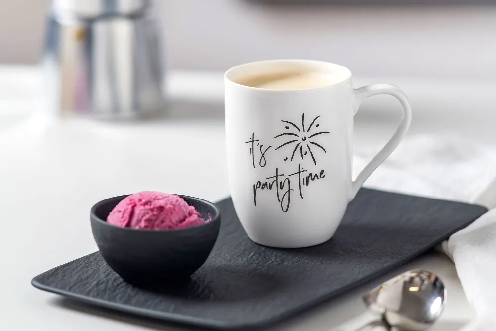 A Statement mug with the text “It’s Party Time” on a tray next to a small black bowl of ice cream. 