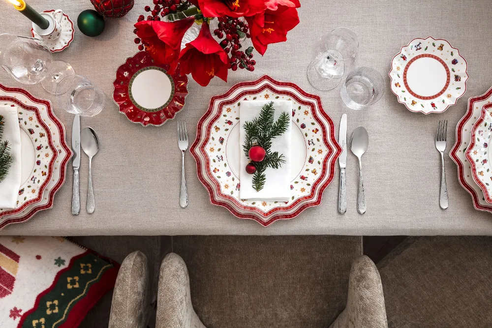 A festive table setting with Toy's Delight plates, cutlery and glasses, neatly arranged on a beige tablecloth.