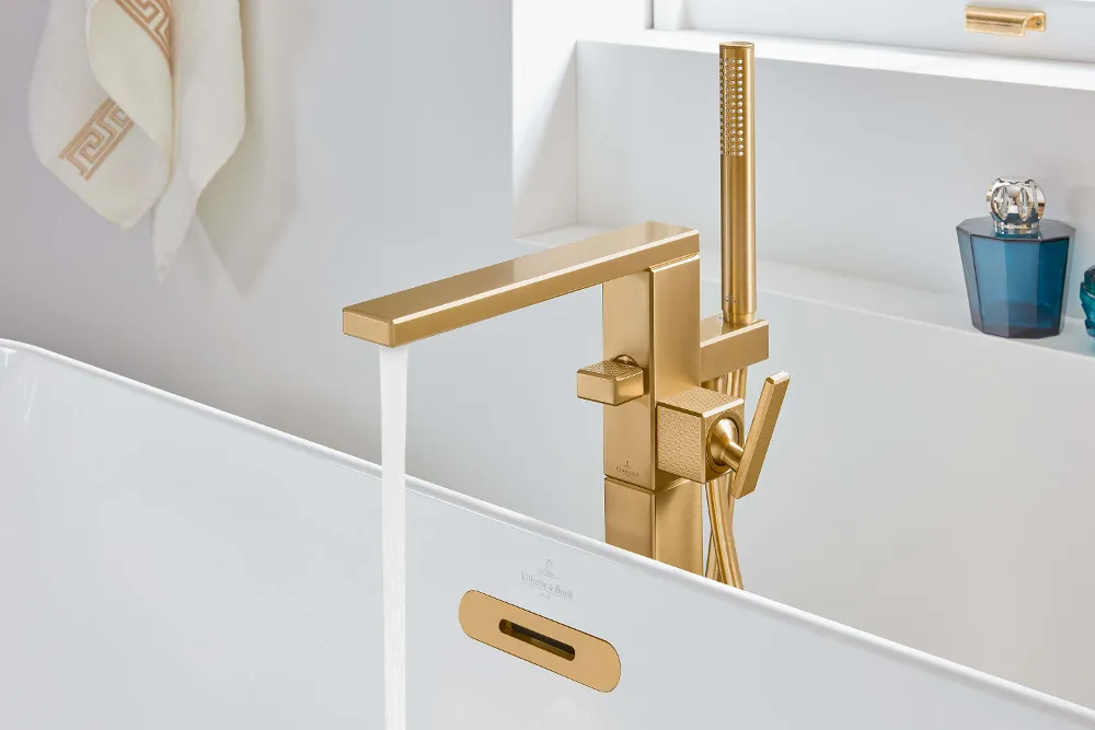 Ein modernes Badezimmer mit einem goldfarbenen Wasserhahn mit fließendem Wasser, einem an der Wand hängenden Handtuch und dekorativen Gegenständen auf dem Regal.