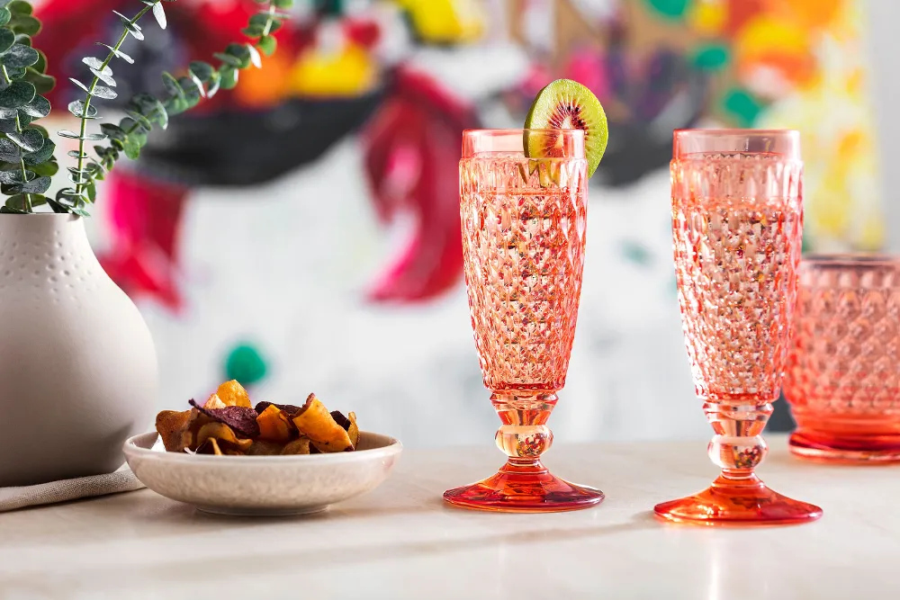 Two orange Boston glasses on a table next to a bowl of fruit.