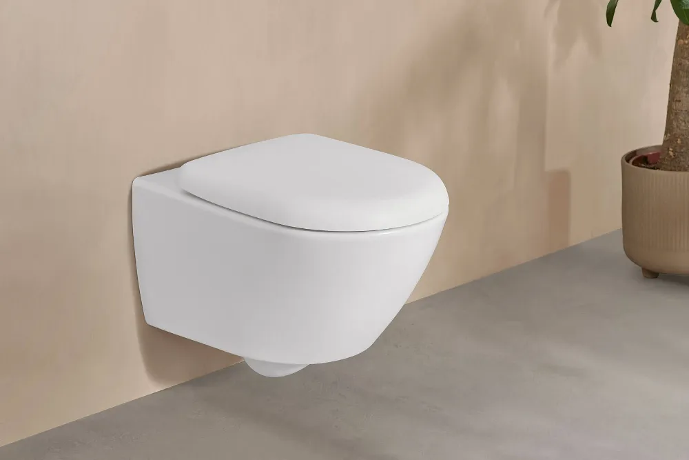 Eine weiße Antao Toilette von Villeroy & Boch in einem eleganten beigen Bad mit Topfpflanze.