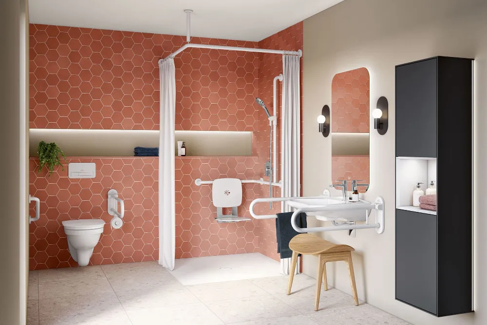 Barrierefreies Badezimmer mit orangefarbenen, sechseckigen Fliesen, einer ebenerdigen Dusche mit Haltegriffen und Klappsitz, einem wandmontierten Waschbecken mit Sicherheitsgeländern, einem hinterleuchteten Spiegel, einer Toilette mit Haltegriffen und Stauraumeinheiten.