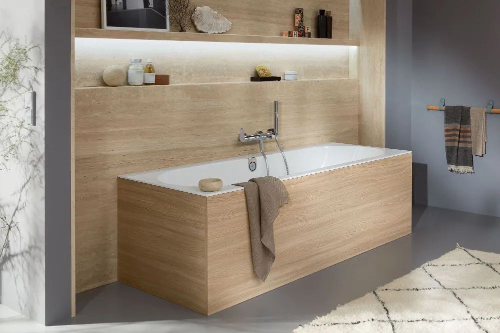 Modern bathroom with a square wood-panelled bath, built-in shelves with decoration and toiletries, a towel hanging at the side and a soft, neutral colour palette.