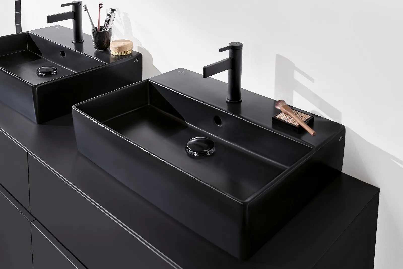 Due lavabi da bagno rettangolari neri di Villeroy & Boch con rubinetti neri opachi su un piano scuro, dotati di utensili da bagno minimalisti.