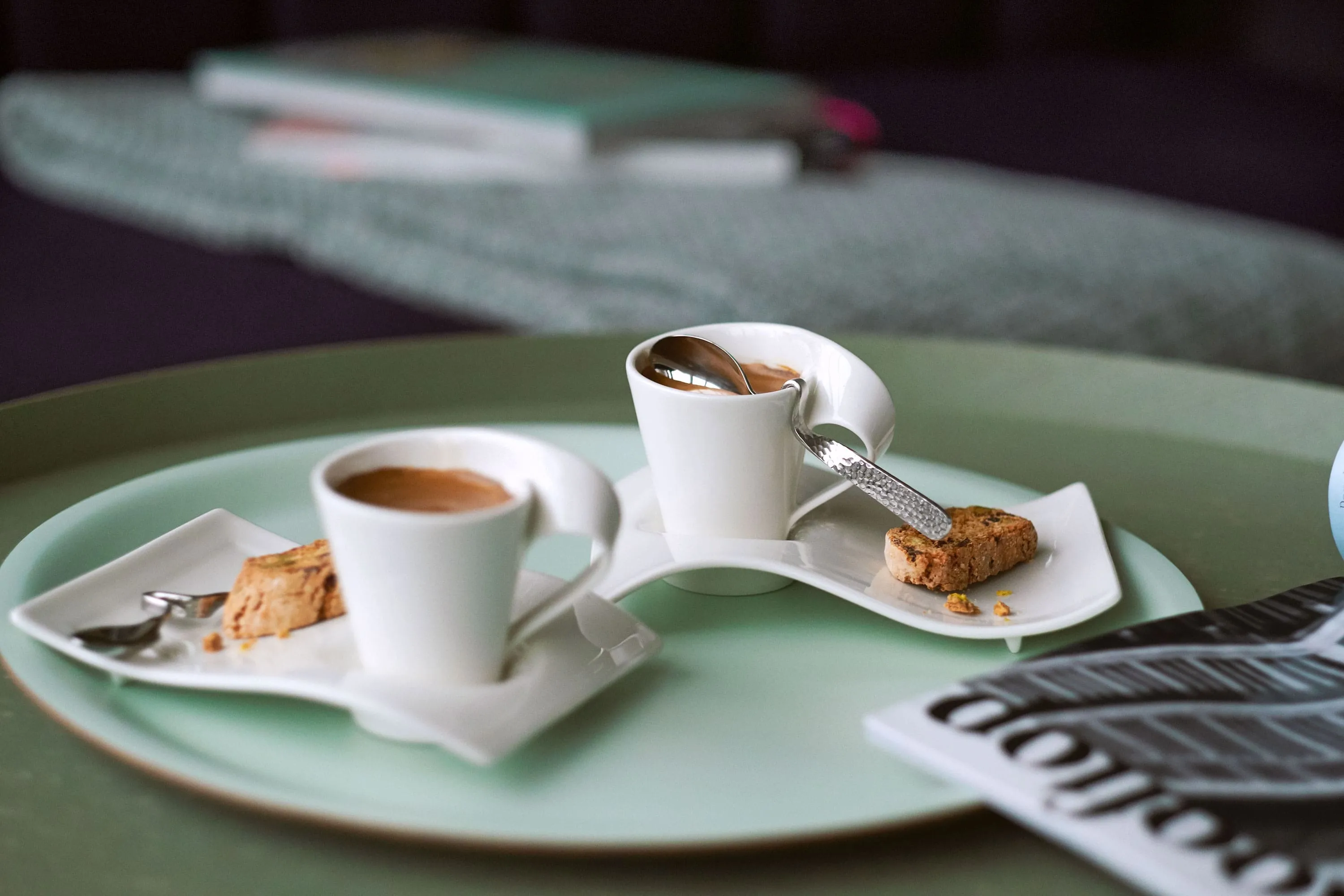 Deux tasses à expresso NewWave avec des cuillère et des sous-tasses, sur un grand plateau vert avec un journal à côté.