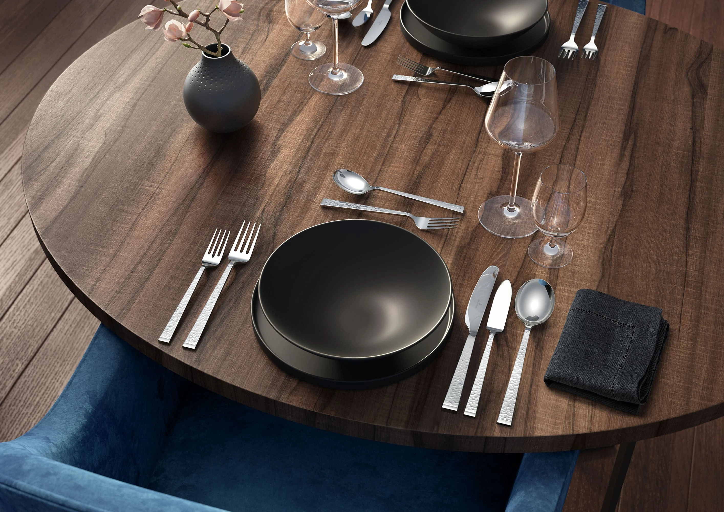 Un tavolo da pranzo in legno apparecchiato con posate Blacksmith, bicchieri La Divina e piatti della La Boule nera di Villeroy & Boch.