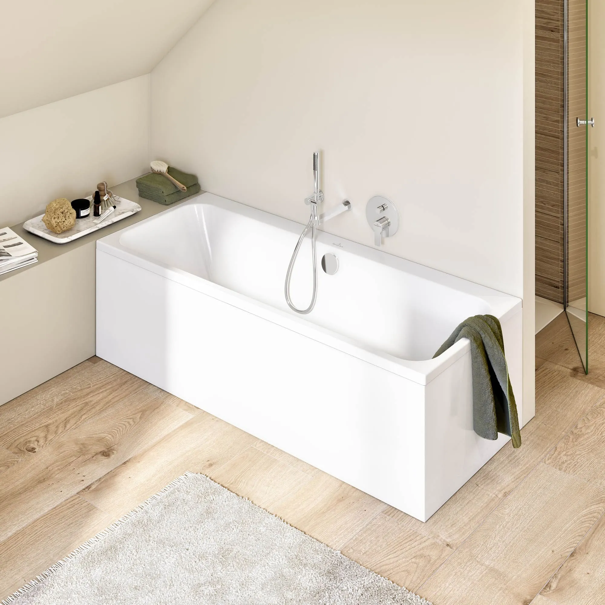 Un bagno moderno con una vasca Architectura rettangolare bianca con un asciugamano verde appeso al bordo. La stanza ha un pavimento in legno chiaro e una parete beige. Accanto alla vasca è presente una mensola con articoli da bagno.