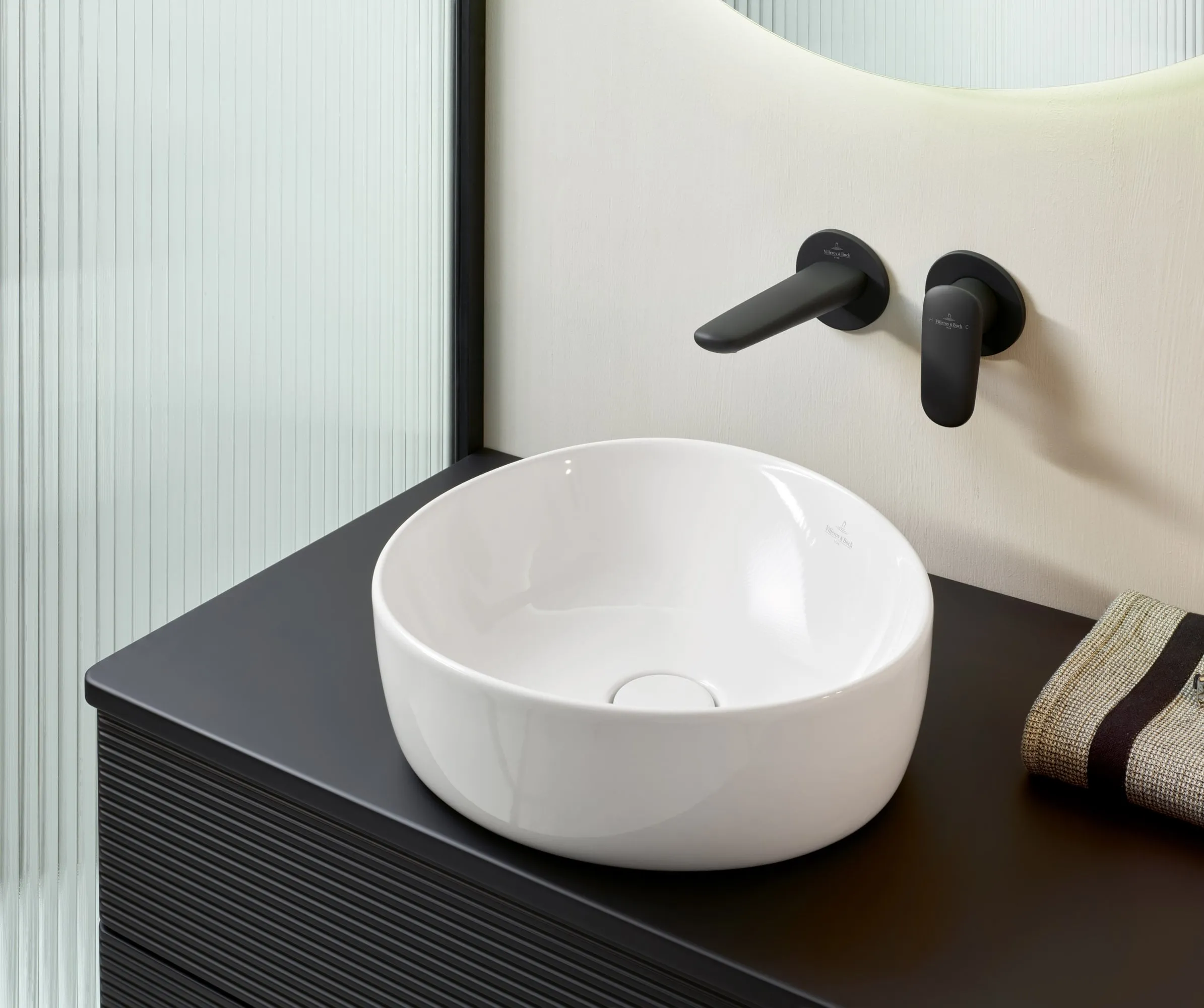 Un espace lavabo moderne Antao de Villeroy & Boch, en noir et blanc, avec une vasque avec une robinetterie en noir mat et un miroir.