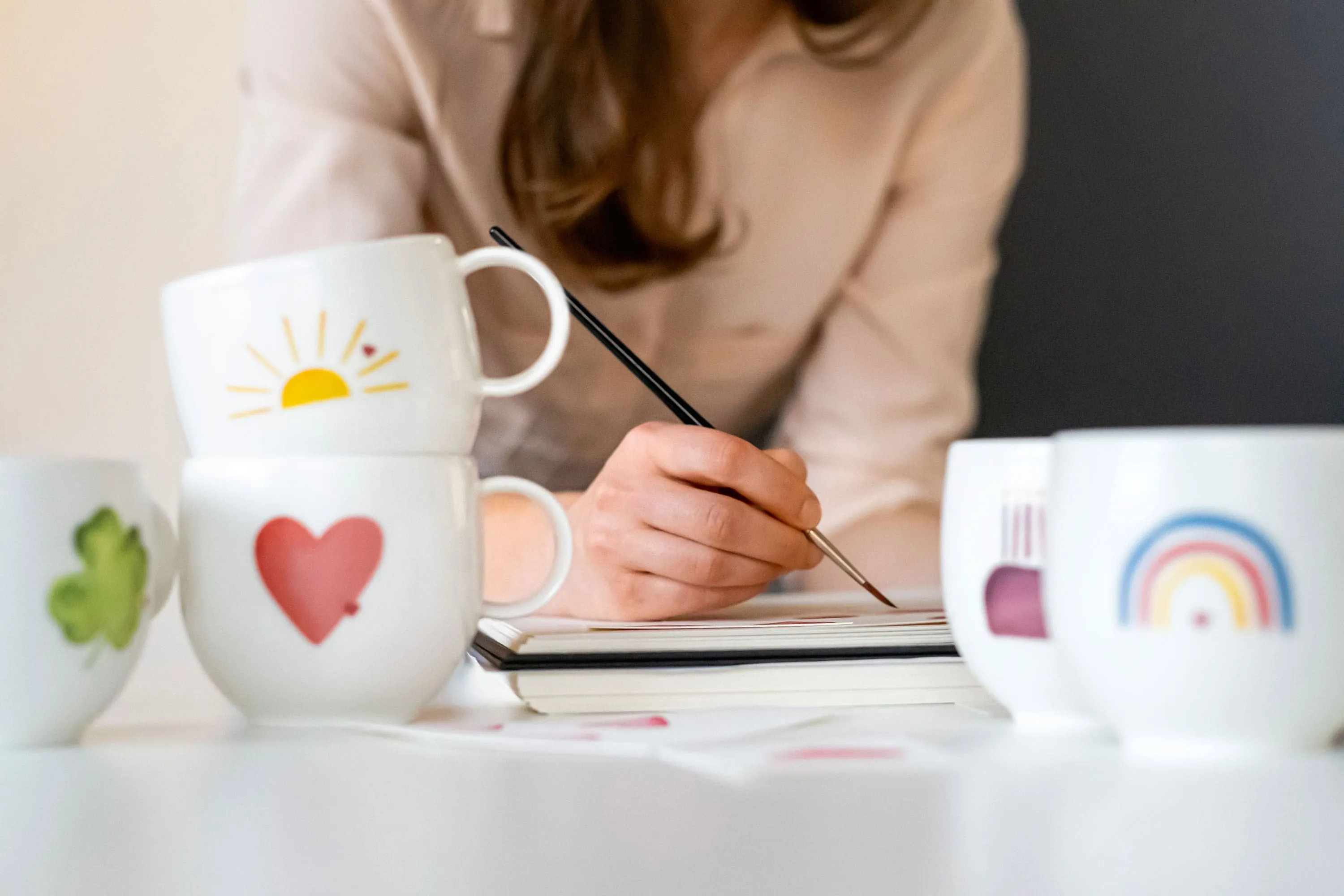  With Love kopjes met verschillende motieven, terwijl een vrouw op de achtergrond schildert.