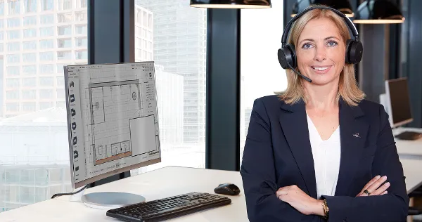 Employée de Villeroy & Boch pour le conseil en salle de bain Une employée est assise à son bureau face à la caméra. En arrière-plan, on peut voir la planification de la salle de bain sur l'écran
