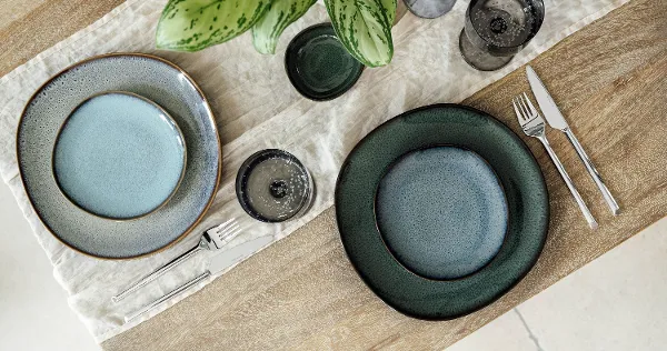 Top-down view of a modern table arrangement featuring dinner and bread plates from Villeroy & Boch’s Lave collections: Lave Vert, Lave Beige, and Lave Glacé. The clean composition highlights the unique reactive glazes and natural textures of each plate on a neutral tabletop, with no food present, emphasizing the artisanal elegance of the stoneware