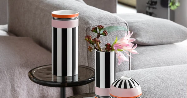 Two black and white striped vases stand on glass tables Two black and white striped vases and a round vessel stand on glass tables next to a grey sofa, flowers in a vase