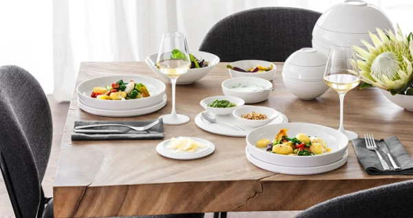 A table set with La Boule with black and grey chairs around it A La Boule table setting with two plates of food, two glasses of white wine, various bowls with side dishes and a flower arrangement with black and grey chairs around the table.